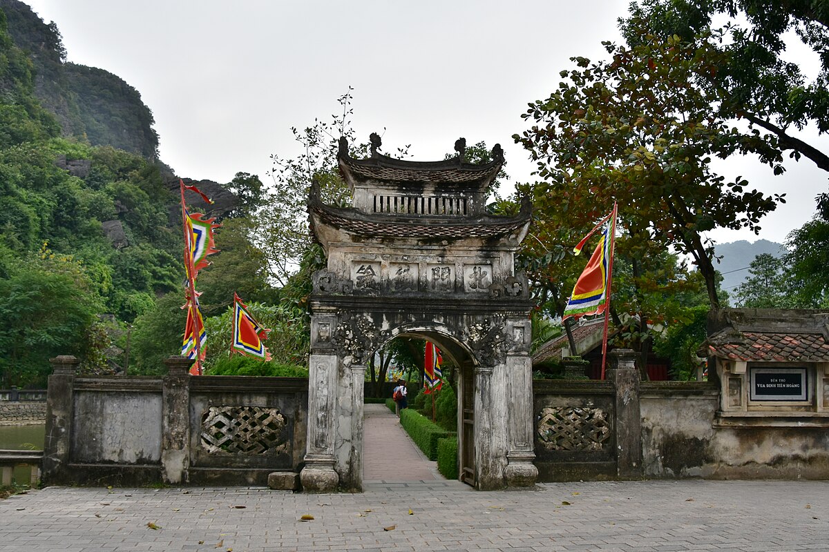 The ornate stone gateway of the ancient capital of Hoa Lu with traditional Vietnamese flags and karst mountain behind