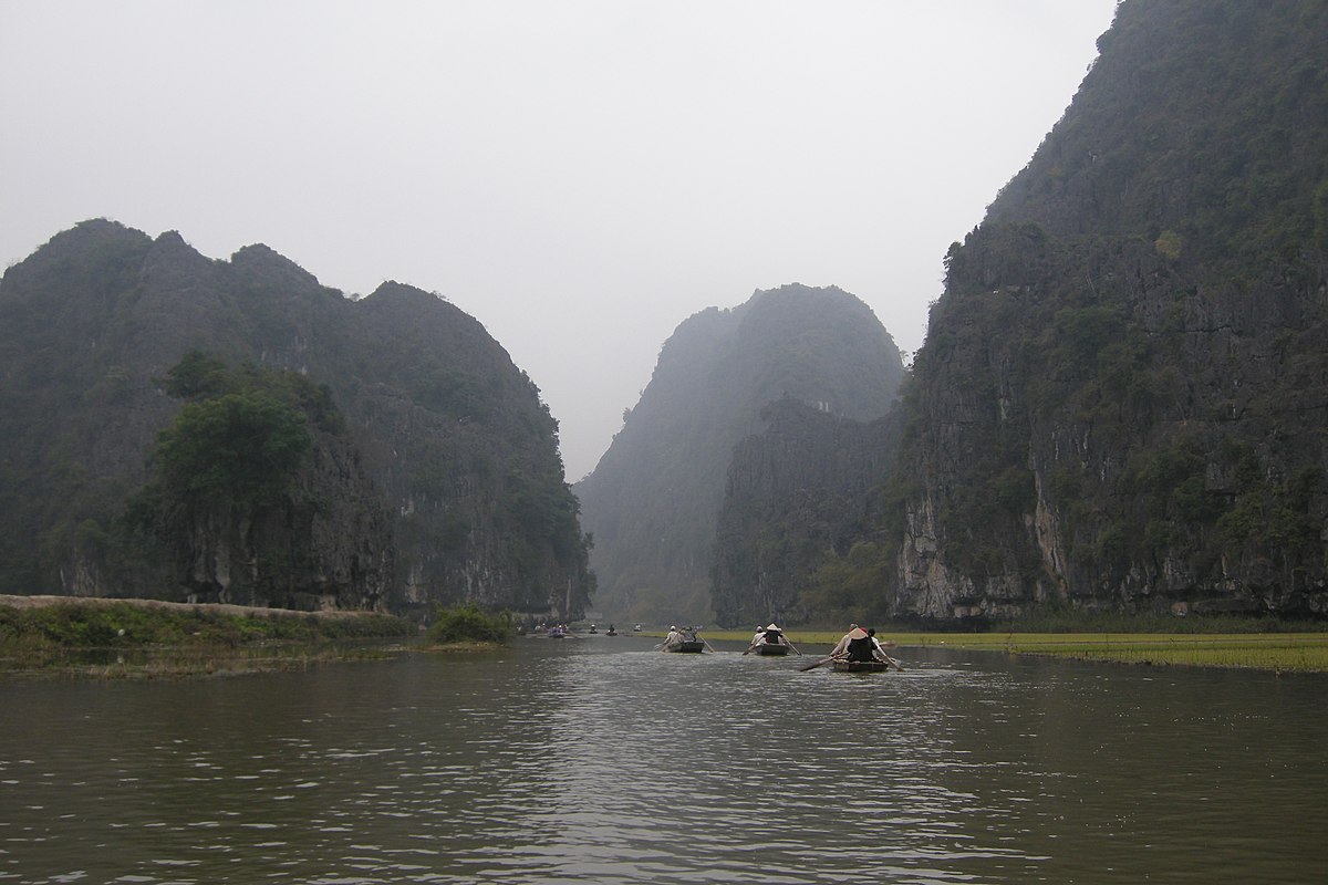 Rowing boats navigating between towering limestone cliffs on the river near Mua Cave, Ninh Binh