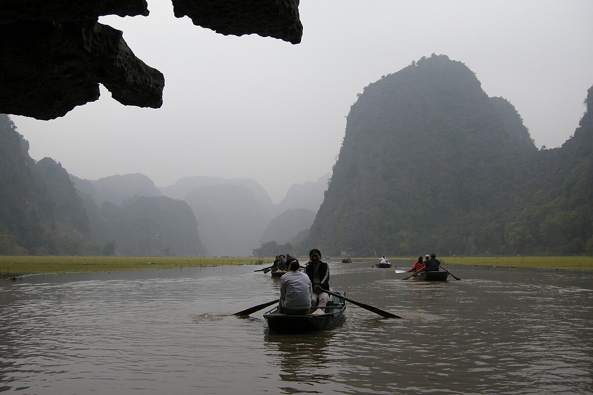 Traditional boats emerging from a cave on the Trang An river with misty karst mountains